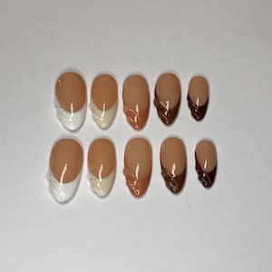 Può includere: Set di dieci unghie finte con vari design. Alcune unghie presentano una french manicure bianca o beige, mentre altre hanno accenti marroni o rosso scuro. Le unghie sono di forma ovale e disposte su sfondo bianco.