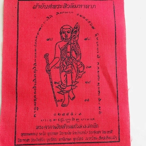 Puede incluir: Un cuadrado de tela roja con texto e ilustraciones en negro. La imagen central es una figura que sostiene un bastón y un bulto. El texto está en escritura no inglesa, con texto adicional alrededor de la figura y en la parte inferior.