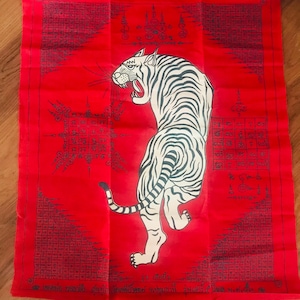 Könnte beinhalten: Rotes Textil mit einer Illustration eines weißen Tigers. Der Tiger ist mit schwarzen Streifen und offenem Maul dargestellt. Aufwendige schwarze Muster und Text umgeben den Tiger und erzeugen ein detailliertes Design.