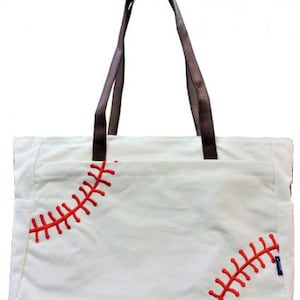 May include: White tote bag with brown handles and red stitching, resembling a baseball. The bag has a rectangular shape with a pocket on the front. The handles are a dark brown colour.