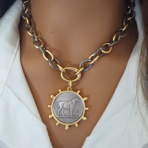 May include: A gold and silver chain necklace with a large, round pendant featuring a silver horse silhouette. The pendant has a gold rim with small, decorative gold balls around the edge.
