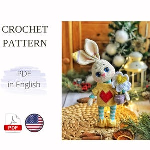 Könnte beinhalten: Häkelanleitung PDF in Englisch für ein weißes Amigurumi-Häschen, das einen Blumentopf hält. Das Häschen trägt ein gelbes Shirt mit einem roten Herzen und eine blau-weiß gestreifte Hose.