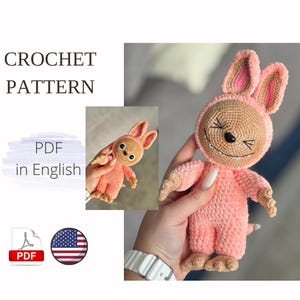 May include: A crocheted pink bunny toy with a smiling face, brown accents, and long ears. The image includes the text "CROCHET PATTERN" and "PDF in English."