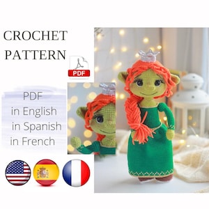 Puede incluir: Patrón de crochet para una muñeca princesa verde con cabello naranja y una corona. El patrón está disponible en formato PDF en inglés, español y francés. La imagen muestra la muñeca con un fondo blanco.