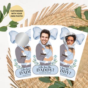 May include: Three rectangular scratch-off cards featuring a cartoon illustration of a person carrying a baby in a carrier. Each card has a blue bow graphic, floral accents, and the text Who has the DADDY? scratch & reveal. One card shows a photo.