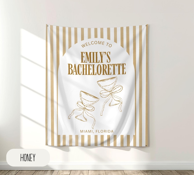Puede incluir: Un tapiz rectangular con fondo blanco y rayas verticales beige. El centro presenta el texto "Welcome to Emily's Bachelorette" con dos copas de champ&aacute;n y la ubicaci&oacute;n "Miami, Florida". La palabra "HONEY" est&aacute; en un rect&aacute;ngulo blanco en la parte inferior.