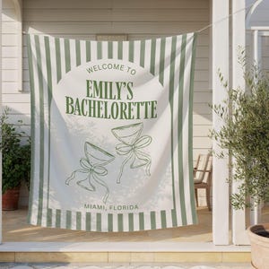 Puede incluir: Una pancarta a rayas blancas y verdes con el texto "Welcome to Emily's Bachelorette" y la ubicaci&oacute;n "Miami, Florida". La pancarta tambi&eacute;n presenta dos dibujos lineales de copas de c&oacute;ctel con lazos.