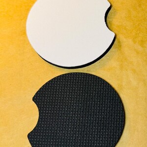 May include: Two round, white and black car coasters. The white coaster is blank and the black coaster has a textured surface.