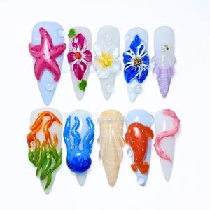 Könnte beinhalten: Ein Set aus zehn stilettoförmigen Press-on-Nägeln mit 3D-Aquatik- und Blumenmotiven. Die Nägel zeigen einen rosa Seestern, leuchtende Blumen, eine blaue Qualle, orangefarbene Algen, einen Koi-Fisch und einen rosa Tentakel mit Wassertropfen.
