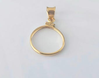 Könnte beinhalten: Ein goldfarbener Anhänger mit kreisförmigem Rahmen und Öse für eine Kette. Der Anhänger hat ein schlichtes, elegantes Design, das für Schmuck geeignet ist. Das Metall hat eine polierte Oberfläche, die das Licht reflektiert.