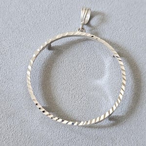 May include: A silver pendant featuring a textured, open circle design. The pendant has a textured surface with diagonal lines and a small loop at the top for a chain. The jewelry is displayed on a gray background.
