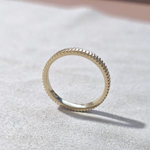 May include: A gold band ring with a textured, ridged design. The ring is simple and elegant.