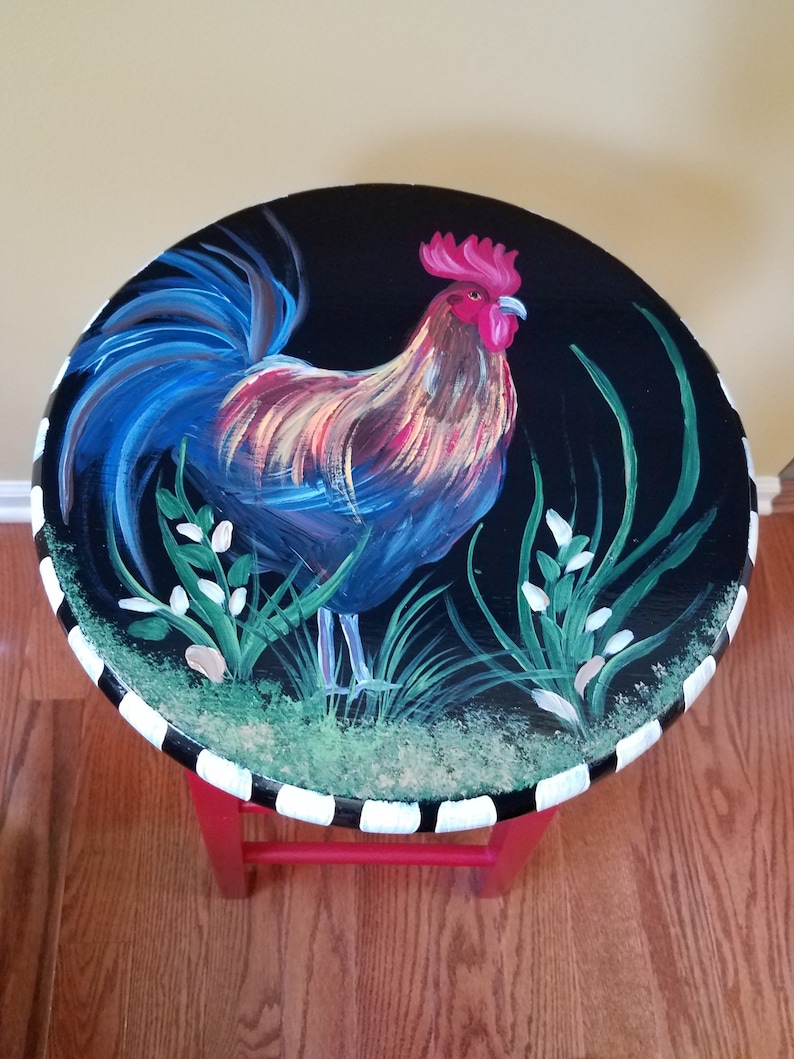 May include: A red painted stool with a black and white striped base. The top of the stool is painted black with a rooster design in shades of blue, red, yellow, and green.