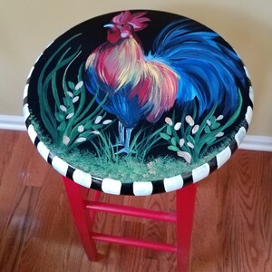 May include: A red painted stool with a black and white striped base. The top of the stool is painted black with a colorful rooster illustration.