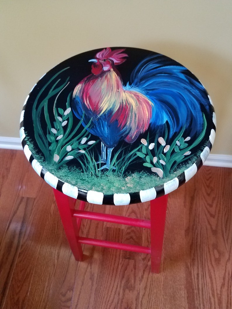 May include: A red painted stool with a black and white striped base. The top of the stool is painted black with a colorful rooster illustration.