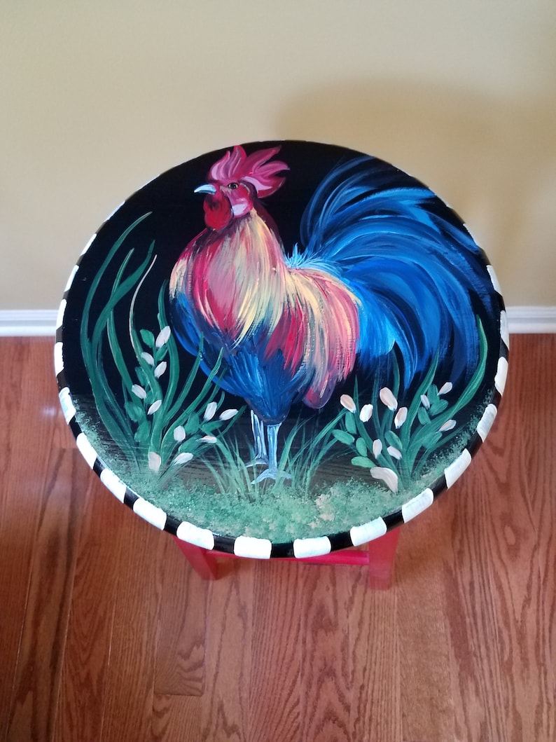May include: A hand-painted wooden stool with a black and white striped base. The top of the stool features a colorful rooster painted on a black background.