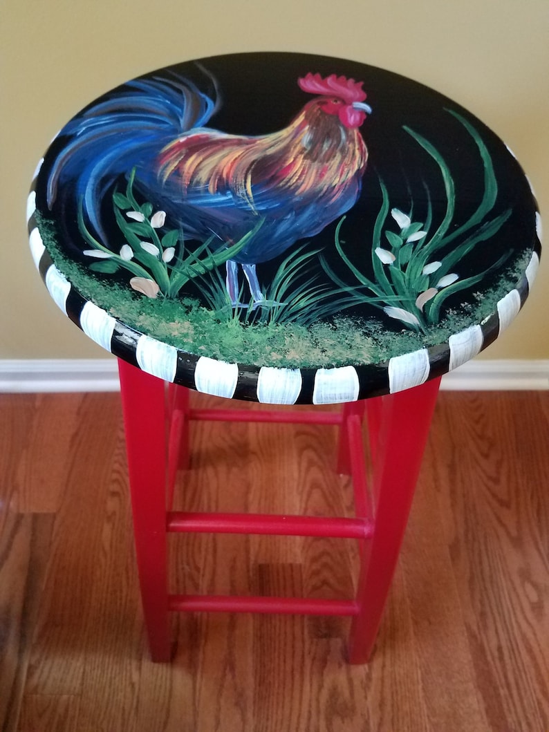 May include: A red painted stool with a black and white striped top. The top features a hand-painted rooster with blue, red, yellow, and green accents.