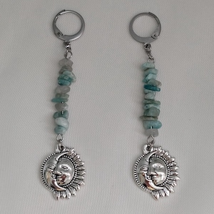 May include: A pair of dangle earrings with silver sun and moon pendants. Each earring has a strand of small, light blue-green stones. The earrings are suspended from a silver leverback clasp.