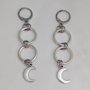 May include: Silver earrings with a series of linked rings suspended from a lever-back clasp. Each earring has a crescent moon charm at the bottom. The earrings have a minimalist design and are made of a silver-toned metal.