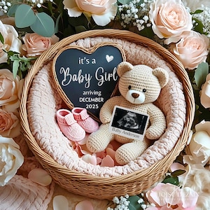 May include: A wicker basket holds a crocheted teddy bear, pink baby booties, and a chalkboard sign that reads "it's a Baby Girl arriving DECEMBER 2025." The bear holds a sonogram photo. The basket is surrounded by pink roses and greenery.