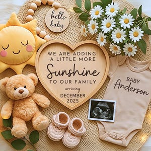 May include: A baby announcement featuring a plush sun, teddy bear, and a heart-shaped wooden sign that reads "WE ARE ADDING A LITTLE MORE Sunshine TO OUR FAMILY arriving DECEMBER 2025." Includes a baby onesie, ultrasound image, and baby shoes.