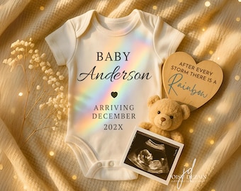 May include: A cream-colored baby onesie with the name "Anderson" and the text "Arriving December 202X". A small teddy bear and a sonogram image are next to the onesie. A wooden heart with the text "After every storm there is a Rainbow" is also present.