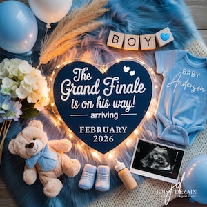 May include: A baby announcement with a blue and white theme. The centerpiece is a heart-shaped sign with the text "The Grand Finale is on his way!" and "February 2026." Includes a onesie, ultrasound image, teddy bear, and balloons.