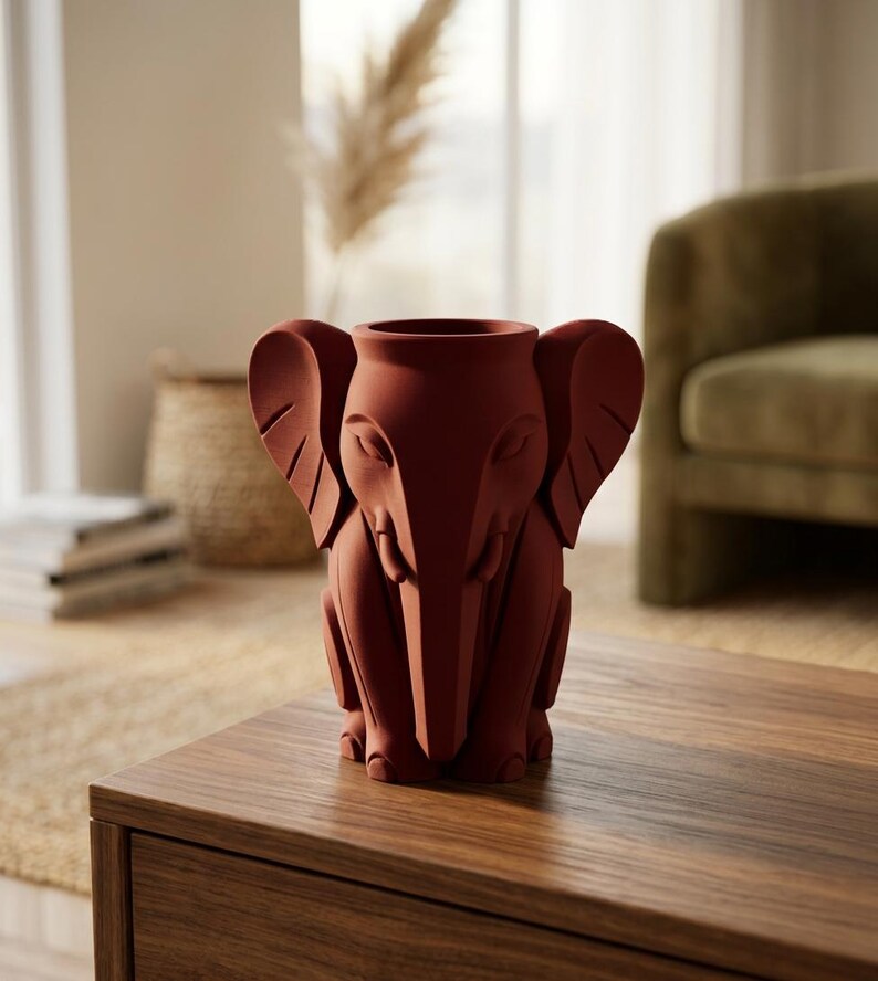 K&ouml;nnte beinhalten: Eine terrakottafarbene Vase in Elefantenform. Die Vase hat gro&szlig;e Ohren, einen R&uuml;ssel und sitzt aufrecht. Die Vase steht auf einem Holztisch in einem Wohnzimmer. Es ist ein dekorativer Gegenstand.