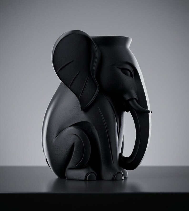 K&ouml;nnte beinhalten: Eine schwarze, elefantenf&ouml;rmige Vase mit glatter, matter Oberfl&auml;che. Die Vase hat einen detaillierten R&uuml;ssel, gro&szlig;e Ohren und eine sitzende Haltung. Das Design ist modern und skulptural, geeignet f&uuml;r die Inneneinrichtung.