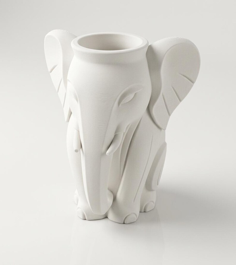 K&ouml;nnte beinhalten: Eine wei&szlig;e, elefantenf&ouml;rmige Vase aus Keramik. Die Vase hat ein detailliertes Design eines Elefantenkopfes, R&uuml;ssels, Ohren und Beine. Die &Ouml;ffnung f&uuml;r die Vase befindet sich auf dem R&uuml;cken des Elefanten. Die Vase ist ein dekorativer Gegenstand.