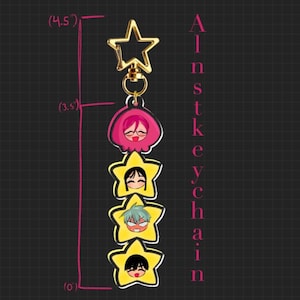 May include: A gold-colored star-shaped keychain with a star-shaped clasp. The keychain features four yellow star-shaped charms with cartoon faces, and a pink charm. The text "Ainst keychain" is printed vertically on the right side. The keychain is 4.5 inches long.