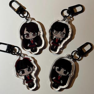 Puede incluir: Cuatro llaveros de acrílico transparente con ilustraciones de estilo anime de un personaje con uniforme escolar. Cada llavero tiene un cierre negro. El personaje tiene cabello negro, un lazo rojo y un uniforme negro y rojo.