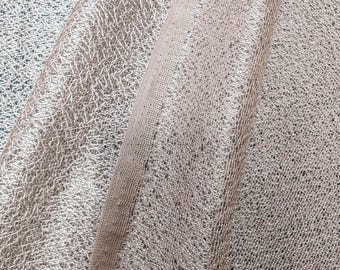 May include: Close-up of a silver metallic fabric with a textured surface. The fabric is folded in half, showing the texture on both sides.