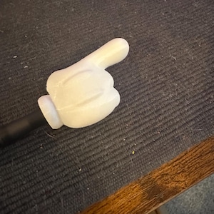 May include: A white plastic hand pointing to the right. The hand is attached to a black stick.