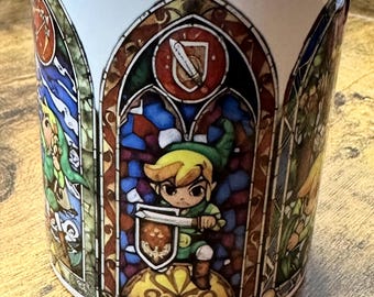 May include: White ceramic mug with a stained glass design featuring Link from The Legend of Zelda. The design includes a shield, sword, and Triforce symbol.