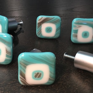 May include: Set of six turquoise and white square glass cabinet knobs with a silver metal base. Each knob features a white center with a brown swirl design.