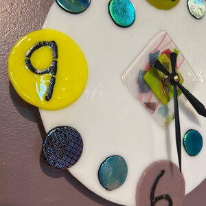 May include: A white clock face with black hands and a diamond-shaped center. The clock face is decorated with colorful glass circles and a yellow circle with the number 9.