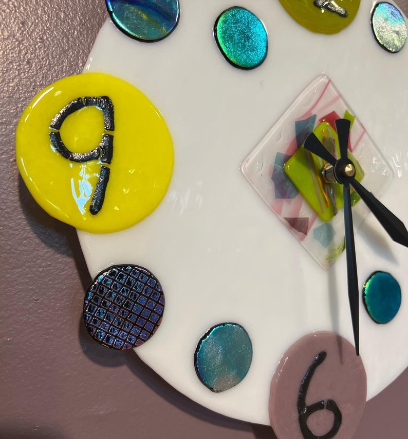 May include: A white clock face with black hands and a diamond-shaped center. The clock face is decorated with colorful glass circles and a yellow circle with the number 9.