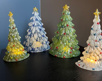 May include: Four ceramic Christmas tree figurines with textured branches and colorful bulb accents. Each tree is topped with a yellow star and features an internal light source that glows from within, creating a warm illumination through the base.
