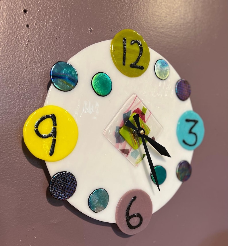 May include: A white circular clock with black hands and colorful glass accents. The numbers 12, 9, 6, and 3 are visible on the clock face.