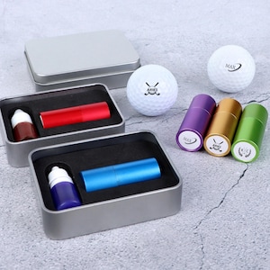 May include: A selection of golf-related items, including golf balls and coloured cylindrical containers. The containers are presented in silver metal boxes with black foam. The golf balls are printed with the word "MAX".