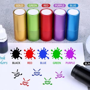 May include: A selection of golf-themed ink stamps in gold, green, red, purple, and blue, with corresponding ink blotches. An ink bottle and a golf ball are also visible. The word "Aries" is printed on the stamps.