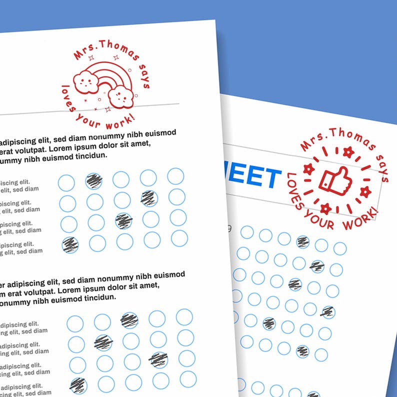 May include: Two white sheets of paper with blue circles and text. One sheet has a red stamp that says "Mrs. Thomas says loves your work!" with a rainbow and clouds. The other sheet has a red thumbs up stamp.