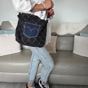 May include: A black quilted denim shoulder bag featuring a prominent dark blue denim pocket on the front with a signature arcuate stitch design. The bag has a wide black fabric strap and is constructed with a diamond-patterned white topstitch.