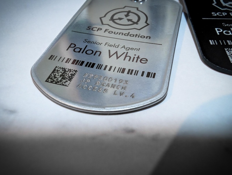 K&ouml;nnte beinhalten: Ein silbernes Metallschild mit dem Text "SCP Foundation" und "Senior Field Agent Palon White" darauf gedruckt. Das Schild hat auch einen Barcode und den Text "#26300193 JIP BRANCH ACCESS LV-4".