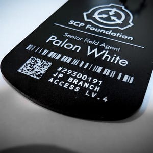 K&ouml;nnte beinhalten: Schwarzes Metalletikett mit wei&szlig;em Text mit der Aufschrift "SCP Foundation", "Senior Field Agent", "Palon White", "#29300191", "JP BRANCH", "ACCESS LV. 4".