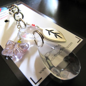 May include: A silver keychain featuring a clear teardrop charm, a lavender butterfly charm, and a silver leaf charm. The keychain is attached to a white card with text that reads "On-line fabricroc etsy.com".