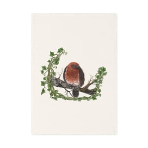 Könnte beinhalten: Ein cremefarbenes, rechteckiges Handtuch mit einer detaillierten Illustration eines Vogels, der auf einem Ast sitzt. Der Vogel hat rotbraune Federn und ist von grünem Efeu umgeben. Das Kunstwerk ist auf dem Handtuch zentriert.