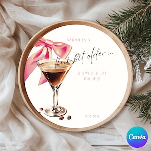 May include: A round wooden tray with a white interior featuring a cocktail illustration and pink bow. Text reads "Sarah is a tiny bit older... & a whole lot bolder!" with the date 10.15.202x. Coffee beans are scattered around the glass.
