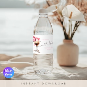 May include: A clear plastic water bottle with a white label featuring a pink bow and a martini illustration. The label reads "A mini bit older & a whole lot bolder". The bottle is topped with a white cap.
